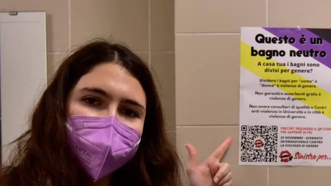 Una giovane mostra un cartello che indica un bagno riservato a chi non si riconosce in nessun genere